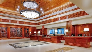 Eine geräumige Lobby mit hoher Decke, Holzvertäfelung und einem großen Kronleuchter. Empfangstresen mit Lampen und Kunstwerken an den Wänden.