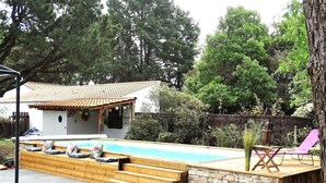 Un patio trasero con piscina, terraza de madera, muro de piedra y un área de patio cubierta.