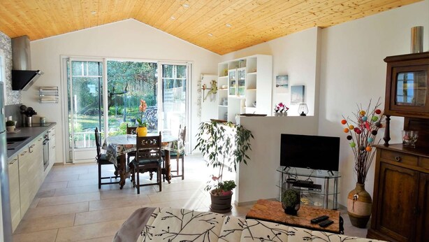 Un amplio salón con techo de madera, una mesa de comedor con sillas, un televisor y una estantería.