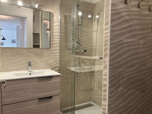 Ein modernes Badezimmer mit einer gläsernen Duschkabine, einem weißen Waschbecken und einem Holzlagerfeld.