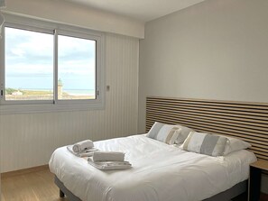 Ein Hotelzimmer mit Bett, Fenster mit Blick auf den Strand und einem hölzernen Kopfteil.