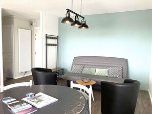 A modern living room with a grey sofa, black chairs, a round table with magazines, and a pendant light. - Drapeau - Saint Gilles Croix de Vie (SAINT GILLES CROIX DE VIE)