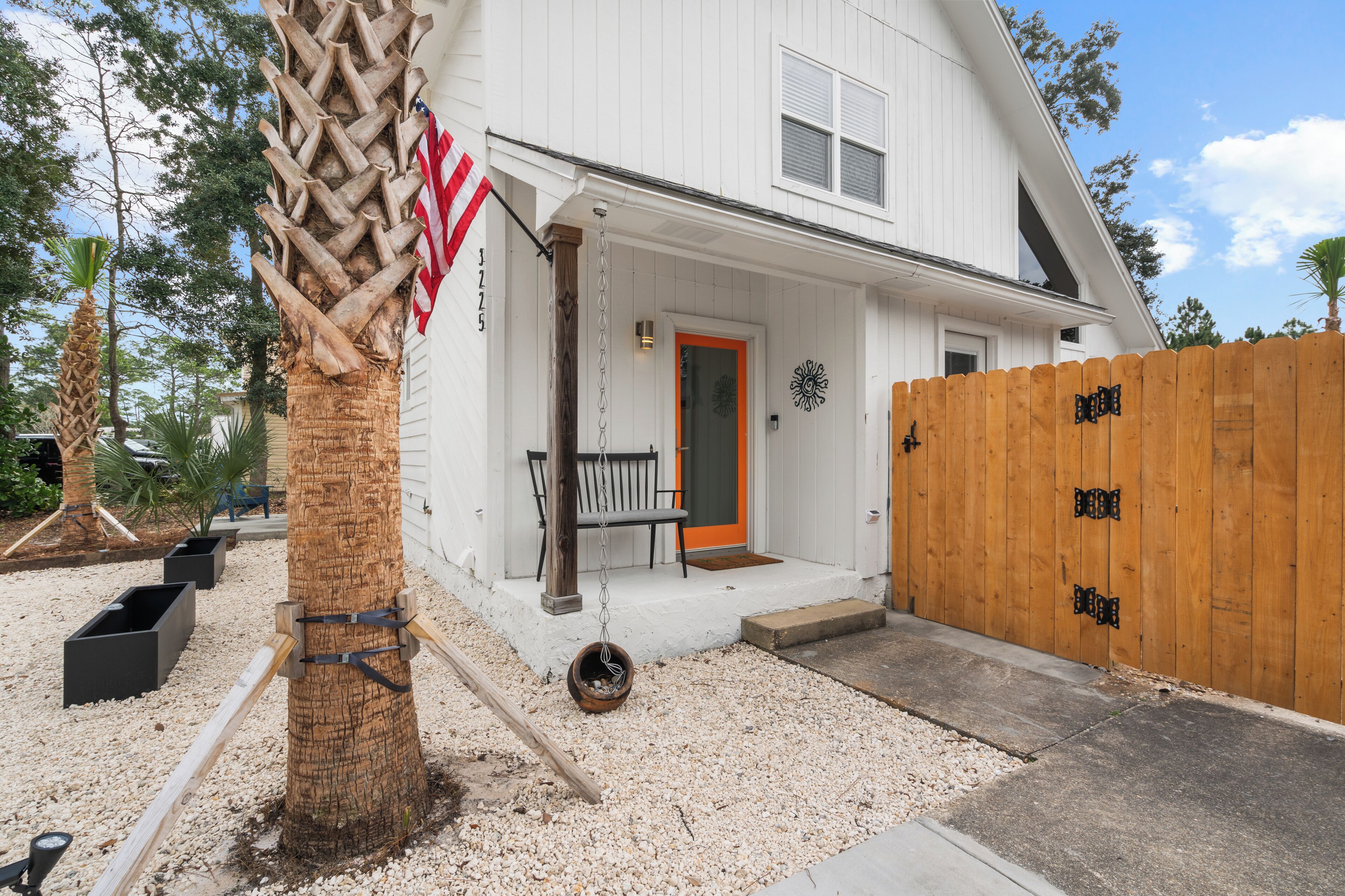 A white two-story house with a wooden fence, a porch with a bench, and a mailbox.