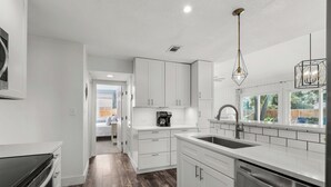 A modern kitchen with white cabinetry, a stainless steel dishwasher, and a wooden floor.