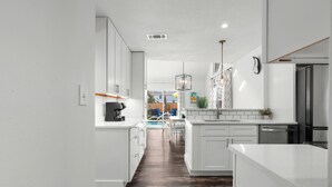 A modern kitchen with white cabinetry, a wooden floor, and a view into a dining area.