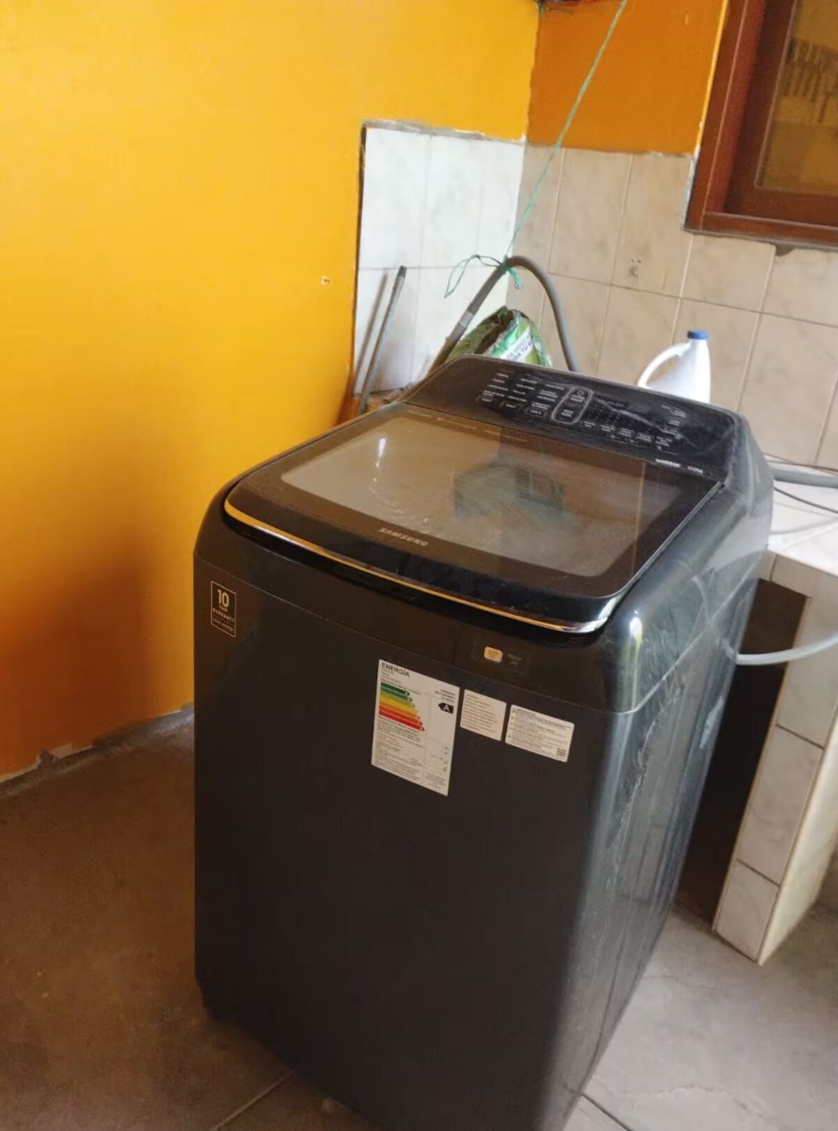 Eine schwarze Waschmaschine mit digitaler Anzeige, einem Stromkabel und einem Wasserfiltersack im Hintergrund.