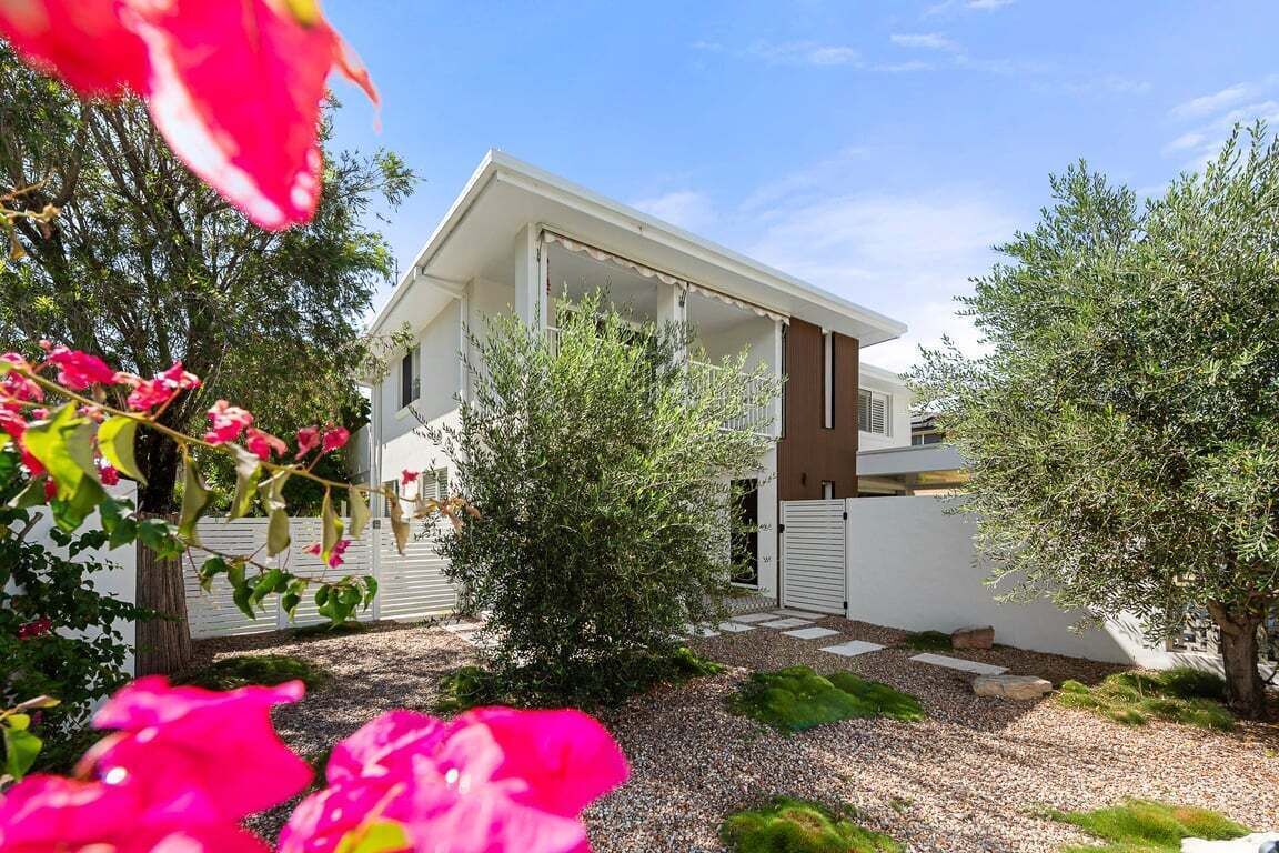 Une maison moderne à l’extérieur blanc, dotée d’un porche abrité et d’une allée gravillonnée.