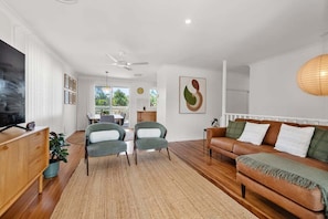 Una sala de estar moderna con piso de madera, un sofá de cuero marrón, dos sillones verdes, un televisor sobre un mueble de madera y un cuadro abstracto grande en la pared.