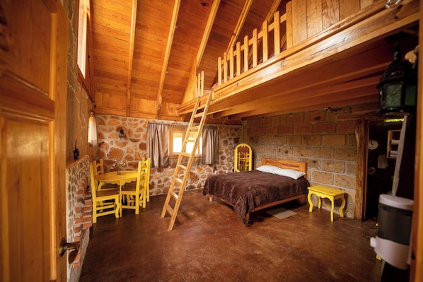 Ein rustikaler Holzraum mit einem Bett, einer Holzleiter, einem Tisch und Stühlen.