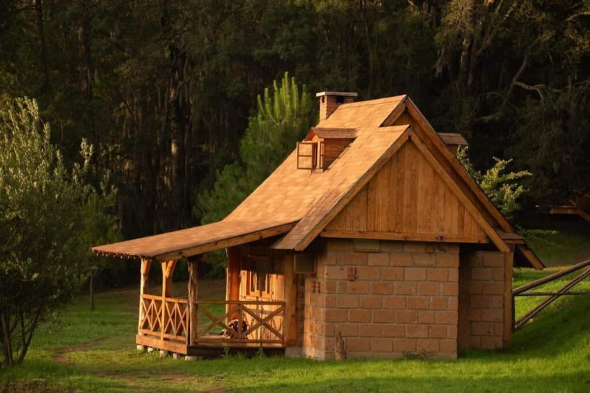 Eine rustikale Holzhütte mit geneigtem Dach, einem Backsteinsockel und einer Holzterrasse.