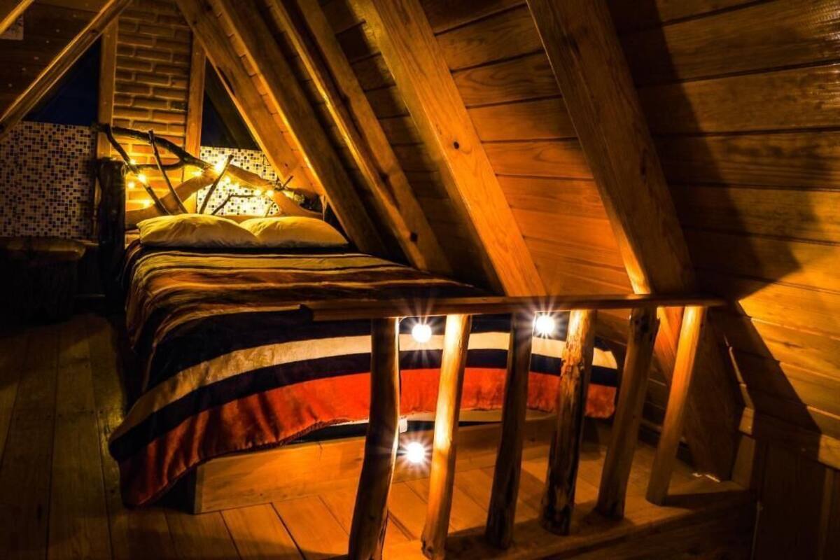 Ein Schlafzimmer im Spitzboden mit Holzbalken, einem Bett mit gestreifter Decke und einem kleinen Tisch mit Stuhl.