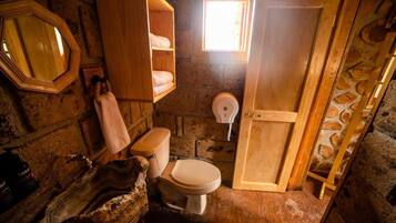 Ein rustikales Badezimmer mit einem Holzbadezimmer-Möbel, einer Toilette und einem kleinen Fenster.