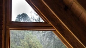 A bedroom with a large window, a bed with patterned bedding, and a view of a forested area. - Canto del Bosque (Nanacamilpa)