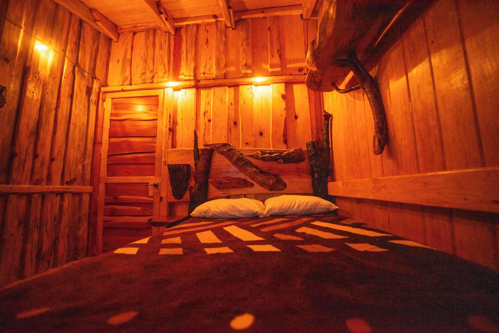 Interior de una cabaña de madera con una cama, almohadas y un rústico cabecero de madera.