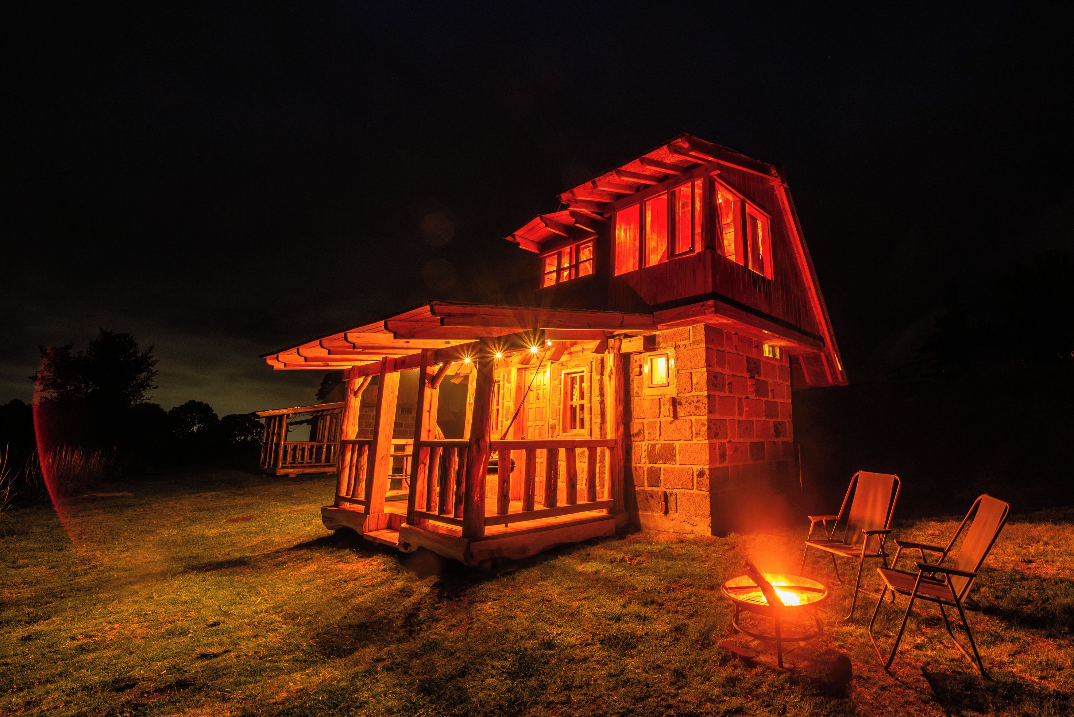 A wooden cabin with a porch and a fire pit, surrounded by grass.