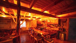 A rustic cabin interior with a wooden dining table and chairs, a stone fireplace, and a kitchen area. - Canto del Bosque (Nanacamilpa)