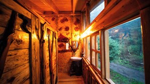 A wooden cabin interior with a rustic design, a wooden bench, a sink, and a window overlooking a forested area. - Canto del Bosque (Nanacamilpa)