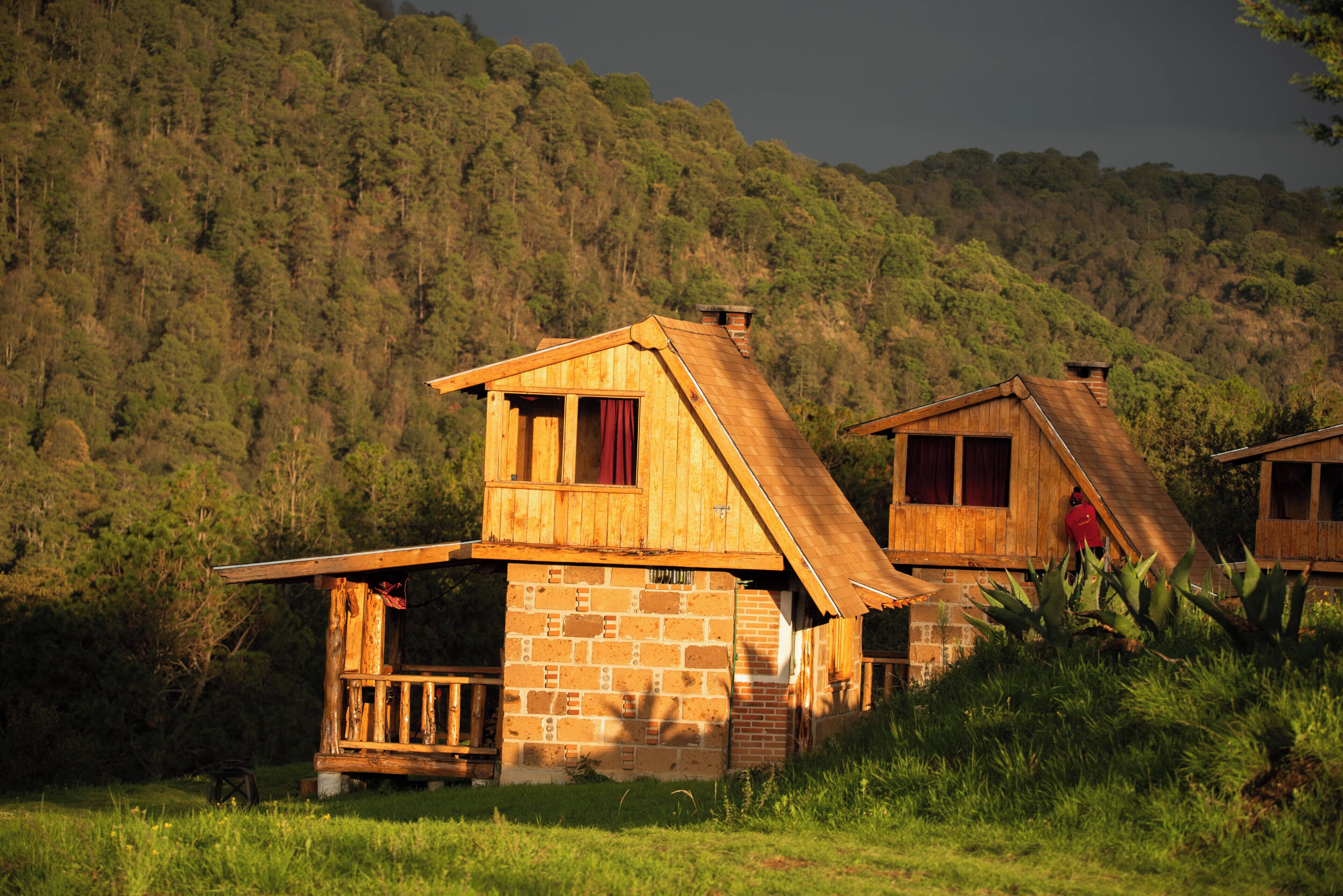 A rustic wooden cabin with a stone foundation, a balcony, and a view of a forested hillside.