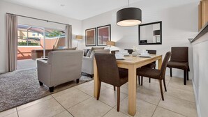 Una habitación de hotel moderna con zona de comedor, sofá, mesa de centro y un gran ventanal con cortinas.