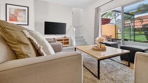 Un salón moderno con sofá, una mesa de centro, televisor y un ventanal con vistas al exterior.