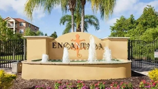 Un letrero con la palabra 'ENGANTADA' y un logotipo de lagarto, rodeado por una fuente y follaje.