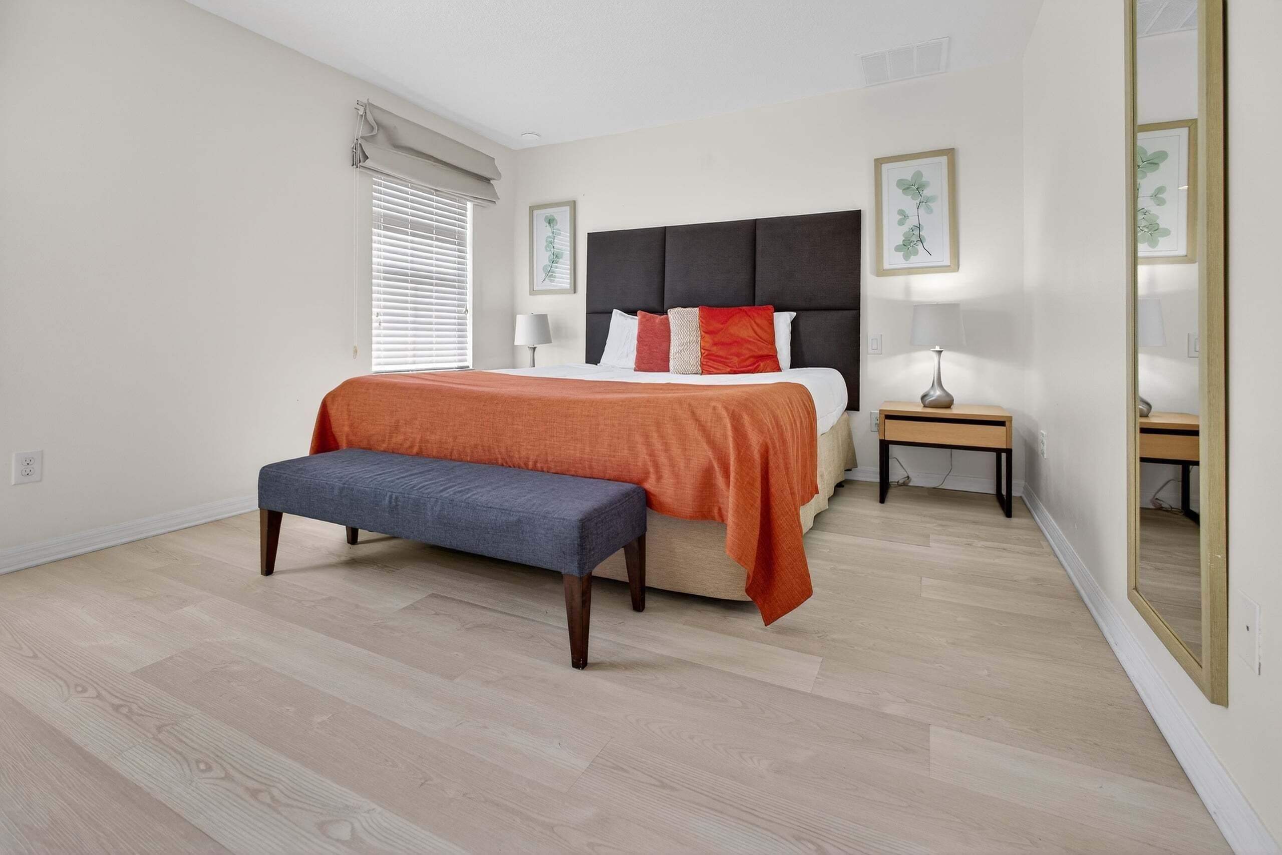 A bedroom with a bed, bench, bedside tables, and a mirror.