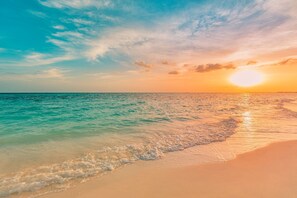 Ein Strand mit klarem türkisblauem Wasser, einem sandigen Ufer und einem Sonnenuntergang im Hintergrund.