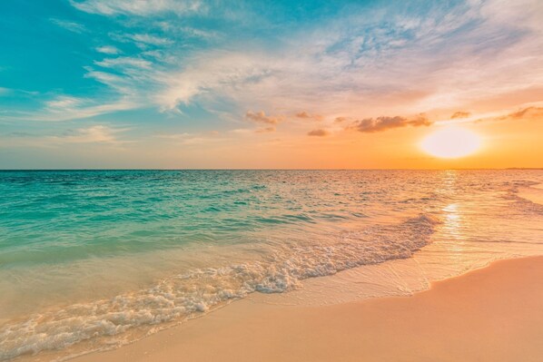 A beach with clear turquoise water, a sandy shore, and a sunset in the background. - The Perdido Pearl (Pensacola)