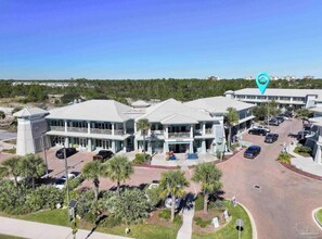 A multi-story hotel with a central courtyard, parking area, and a view of the surrounding landscape. - The Perdido Pearl (Pensacola)