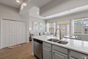 A modern kitchen with a built-in dishwasher, a large island with a sink, and a dining area with a table and chairs. - The Perdido Pearl (Pensacola)