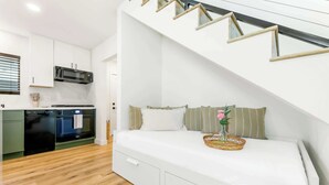A modern apartment with a kitchen, a white bed with storage drawers, and a staircase with a glass railing. - PB New Build - Steps to Sand & Surf (San Diego)