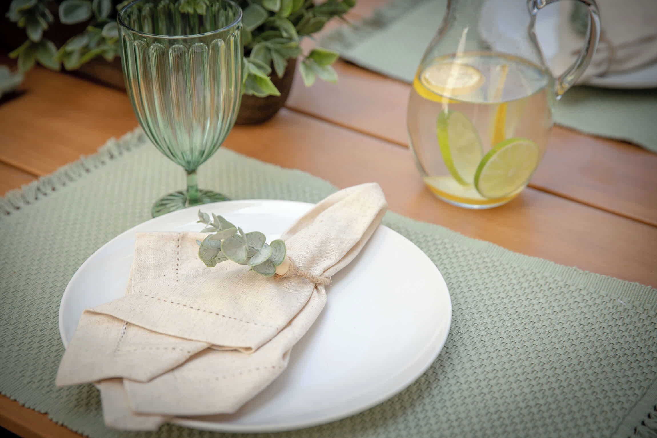 A plate with folded napkins, a glass of water with lime slices, and a glass pitcher on a wooden table with a green placemat.
