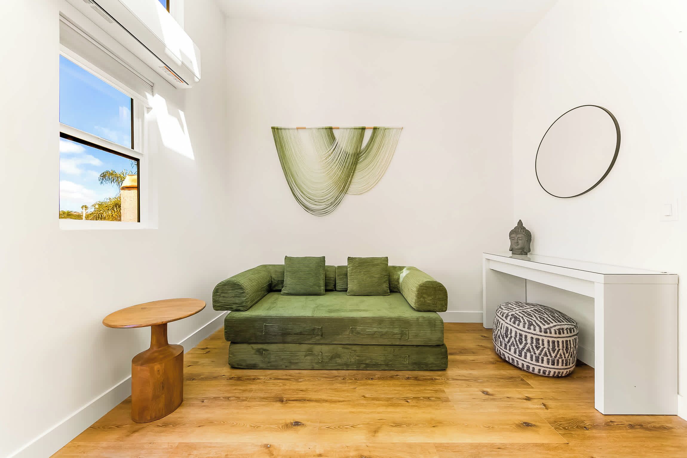 Ein kompakter Wohnbereich mit einem grünen Sofa, einem runden Tisch und einem gemusterten Pouf.
