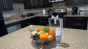 A kitchen with dark cabinets, a stainless steel microwave, a coffee maker, and a fruit basket on the counter. - The Prestige 3BR/2BA Place Near Airport and Mall (McAllen)