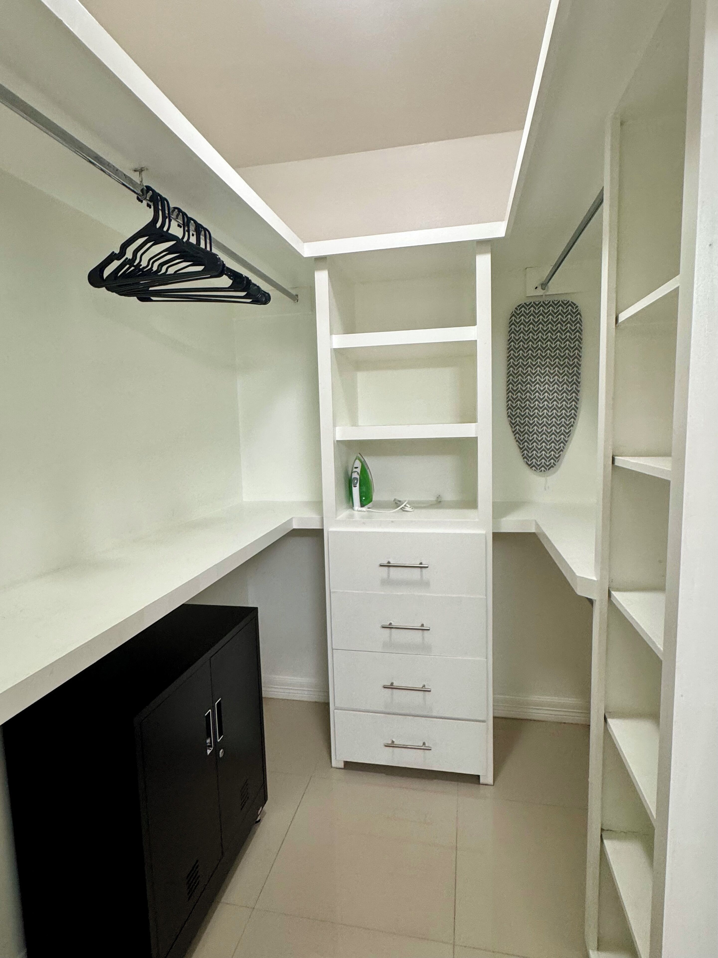 A walk-in closet with white shelving, a black cabinet, and an ironing board.