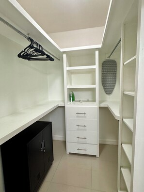 Ein begehbarer Kleiderschrank mit weißen Regalen, einem schwarzen Schrank und einem Bügelbrett.