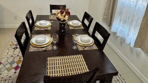 A dining area with a dark wooden table set for six, surrounded by chairs. A decorative wall piece hangs above the table, and a chandelier is visible on the ceiling. - The Prestige 3BR/2BA Place Near Airport and Mall (McAllen)
