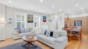 A modern living room with a sofa, a coffee table, and a dining area with a table and chairs. - Elenora history in the heart of town (Queenscliff)