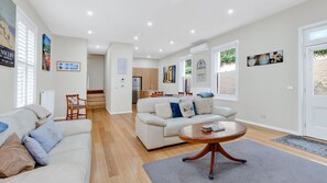 A modern living room with a sofa, a coffee table, and a dining area with a kitchen in the background. - Elenora history in the heart of town (Queenscliff)