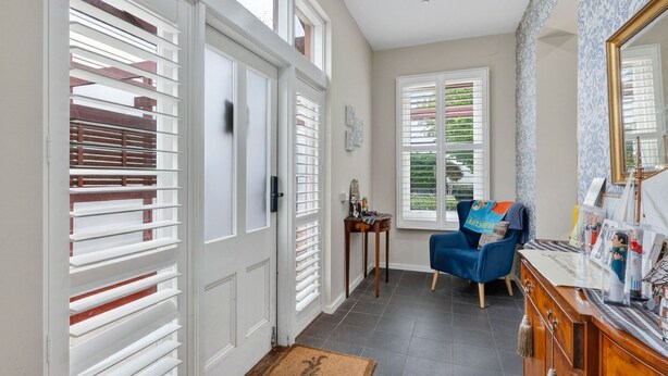 Un couloir avec des portes blanches, une chaise bleue, une petite table ornée de quelques objets décoratifs et un miroir accroché au mur.