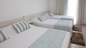 Habitació d'hotel amb tres llits, una finestra amb cortines i un aire condicionat.