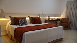 Una habitació d'hotel amb llit, almoinos, una cadira, escriptori i làmpada.