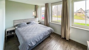 A bedroom with a bed, nightstands, a window with curtains, and a view of the outside.