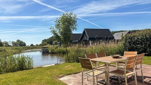A riverside outdoor seating area with a table and chairs, a boat docked on the water, and a building in the background. - Pet friendly home in Witmarsum with WiFi (Witmarsum)