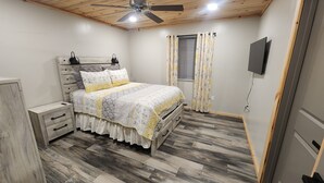 A bedroom with a bed, nightstands, a ceiling fan, a TV, and a window with curtains.