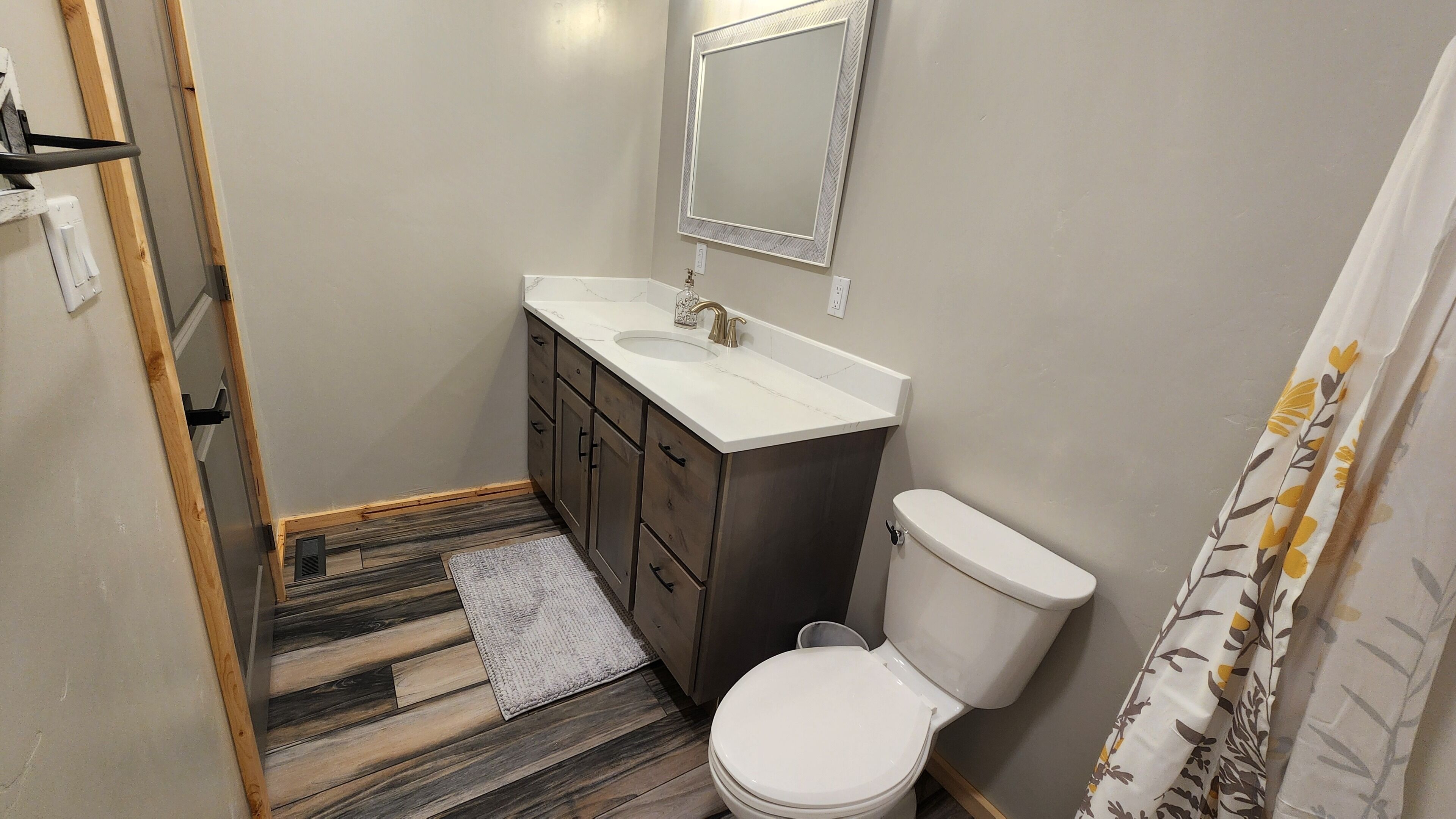 A compact bathroom with a wooden floor, a white sink, a toilet, and a mirror above the sink.