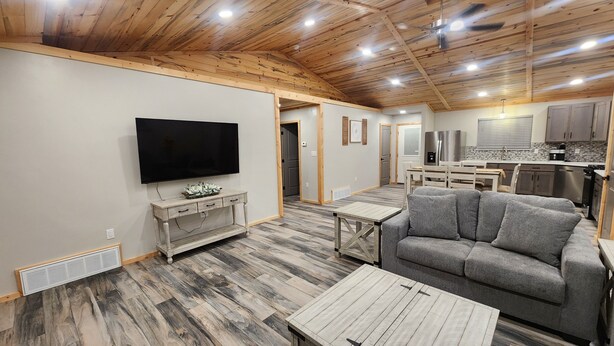 A spacious living area with a flat-screen TV, a grey sofa, and a wooden dining table.