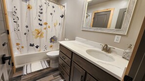 A bathroom with a white sink, a mirror, a toilet, and a shower curtain with floral patterns.