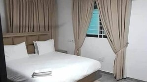 Ein Schlafzimmer mit einem großen Bett, einem Deckenventilator, cremefarbenen Vorhängen und einem Fenster mit Blick.