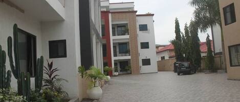 A courtyard with a paved walkway, potted plants, and a parked car.
